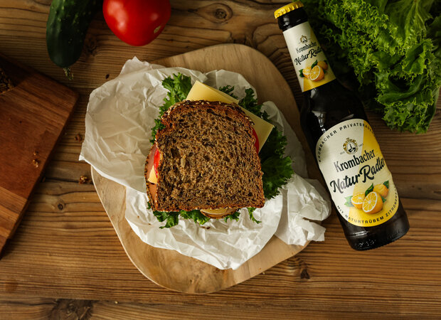 Ein Bergsteiger-Sandwich mit Käse, Schinken, Salat und Tomaten auf einem Holzbrettchen.