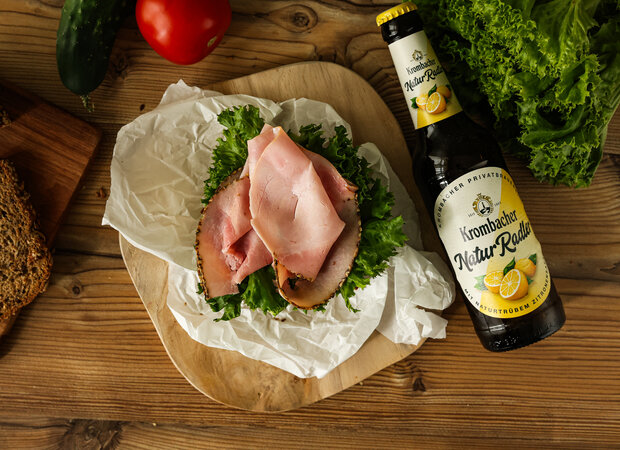 Ein Sandwich mit Schinken und Salat auf einem Holzbrettchen.