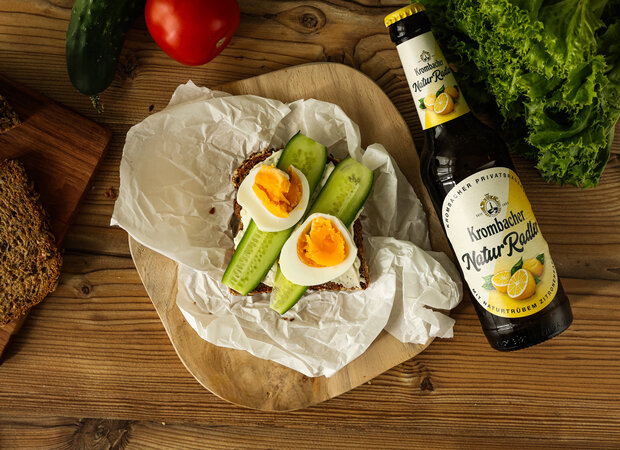 Ein Sandwich mit Gurken und Ei auf einem Holzbrettchen.