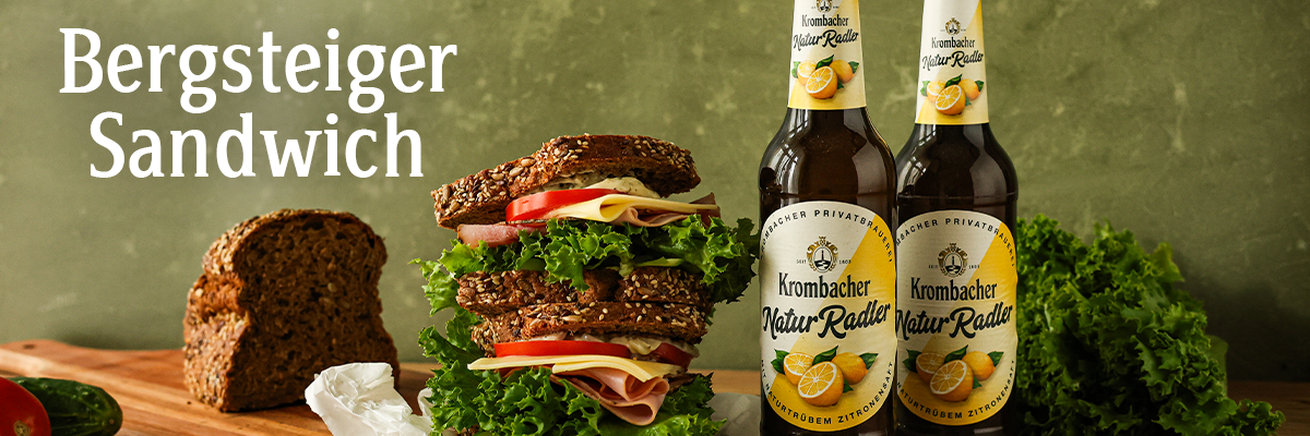 Ein Bergsteiger-Sandwich mit Käse, Schinken, Salat und Tomaten auf einem Holzbrettchen.