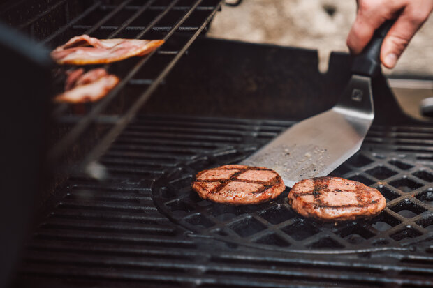 Auf einem Grill werden Patties gewendet.