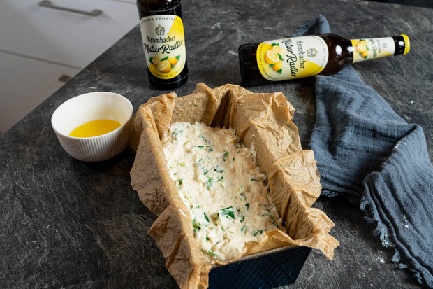 Die Teigmasse liegt in einer Brotbackform mit Backpapier.