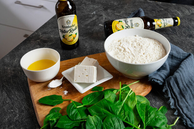 Eigelb, Feta-Käse und Mehl stehen in unterschiedlichen Schüsseln auf einer Holzplatte.