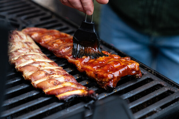 Die Rippchen werden auf einem Grill mit Marinade bestrichen