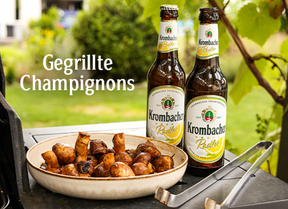 Eine Schale mit gegrillten Champignons neben einem Grill und Krombacher Radler.