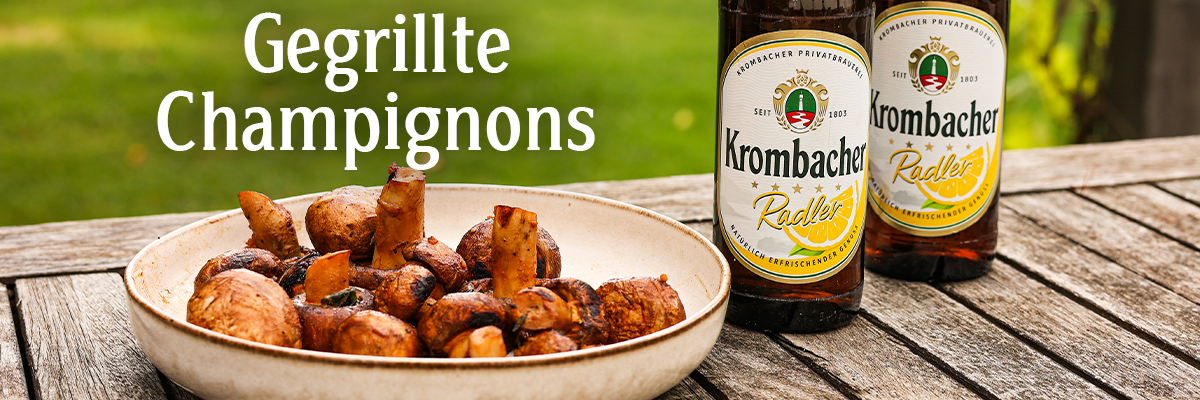 Eine Schale mit gegrillten Champignons neben einem Grill und Krombacher Radler.