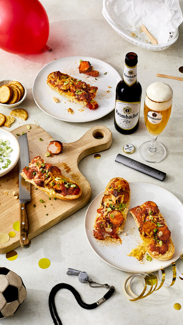 Teile eines selbstgemachten Currywurst - Baguettes auf einer Holzplatte und einem Teller.