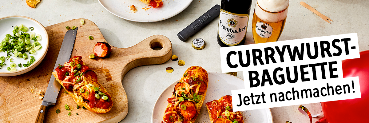 Teile eines selbstgemachten Currywurst - Baguettes auf einer Holzplatte und einem Teller.