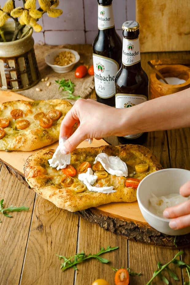 Eine Hand legt Mozzarella aus einer weißen Schüssel auf die Teigteile.
