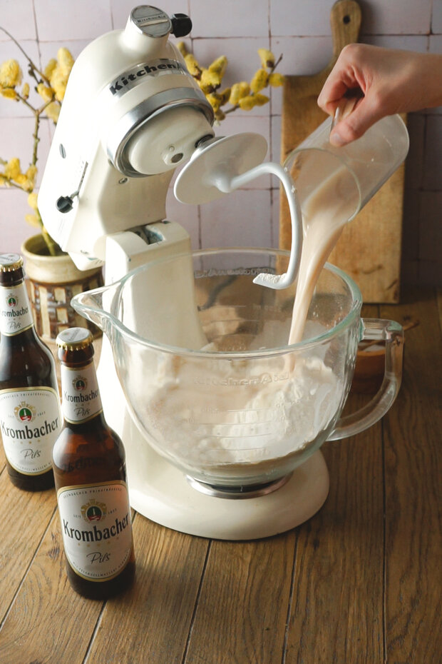 Zum Teig im durchsichtigen Messbecher wird eine Flüssigkeit hinzugegeben.