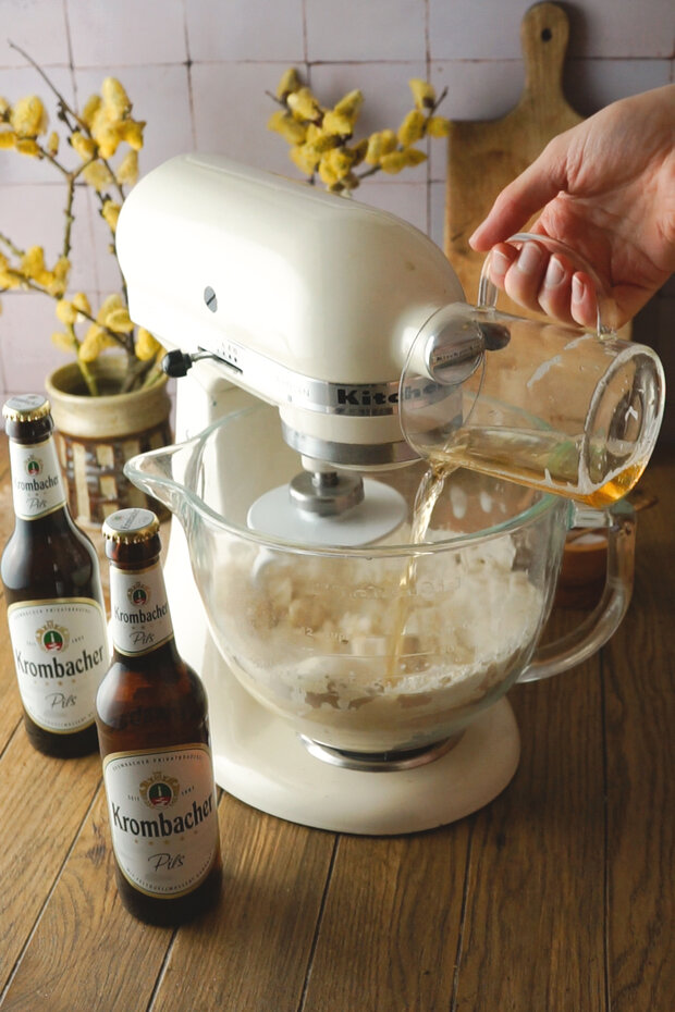 Eine Hand gießt Flüssigkeit in den durchsichtigen Messbecher, in dem der Teig ist.