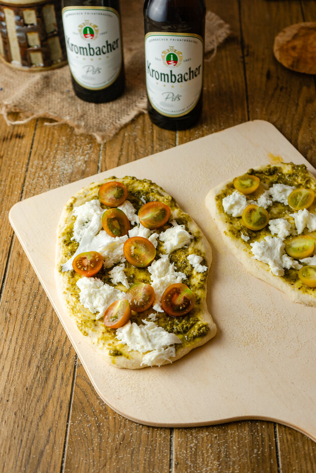 Schafskäse, Tomaten und Pesto sind auf dem Teig verteilt.