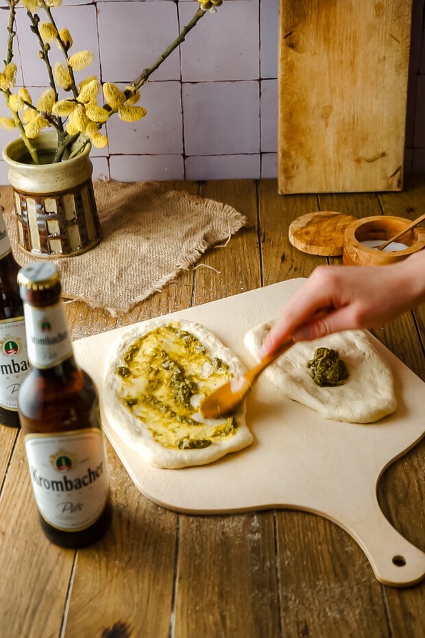 Eine Hand streicht Pesto mit einem Löffel über den Teig.
