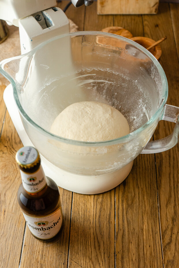 Teig in einem durchsichtigen Messbecher, darunter eine Küchenmaschine und ein Tischtuch. 