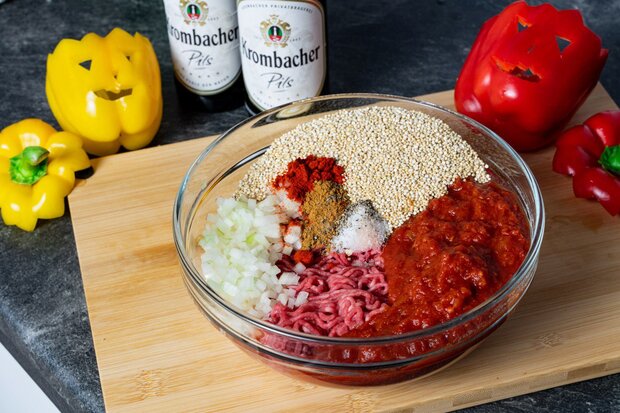 Hackfleisch und Gewürze liegen in einer Schüssel auf einem Holzbrett.