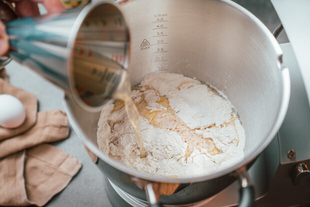 Dem sich in der Rührschüssel befindende Teig wird Wasser hinzugefügt.