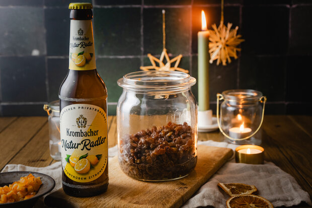 Ein Glas Rosinen steht mit einem Krombacher Natur Radler auf einem Holzbrett.