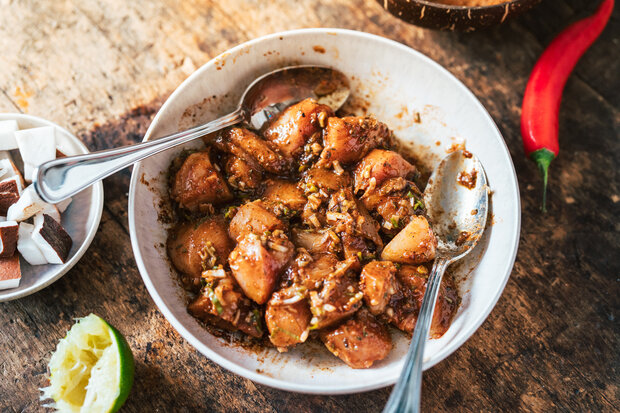 Die Hähnchenstücke liegen in der Marinade mit zwei Löffeln.
