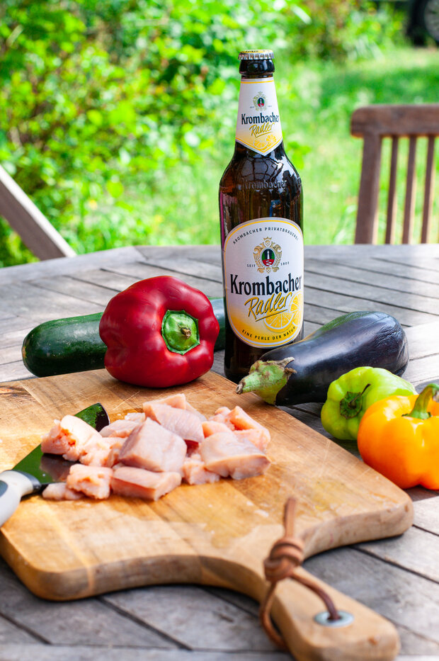 Geschnittener Lachs auf einem Holzbrett, umgeben von Gemüse und einem Krombacher Radler.