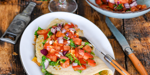 Ein vegan herzhaft gefüllter Crepe mit Tomaten Salsa auf einem Holztisch.