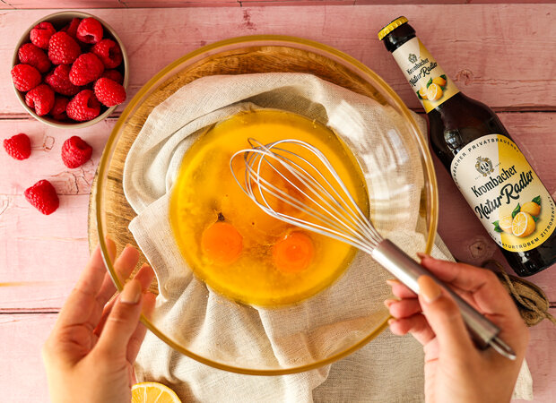 Mehrere Eigelbe in einer durchsichtigen Schüssel, die von einer Hand mit einem Schneebesen umgerührt wird.