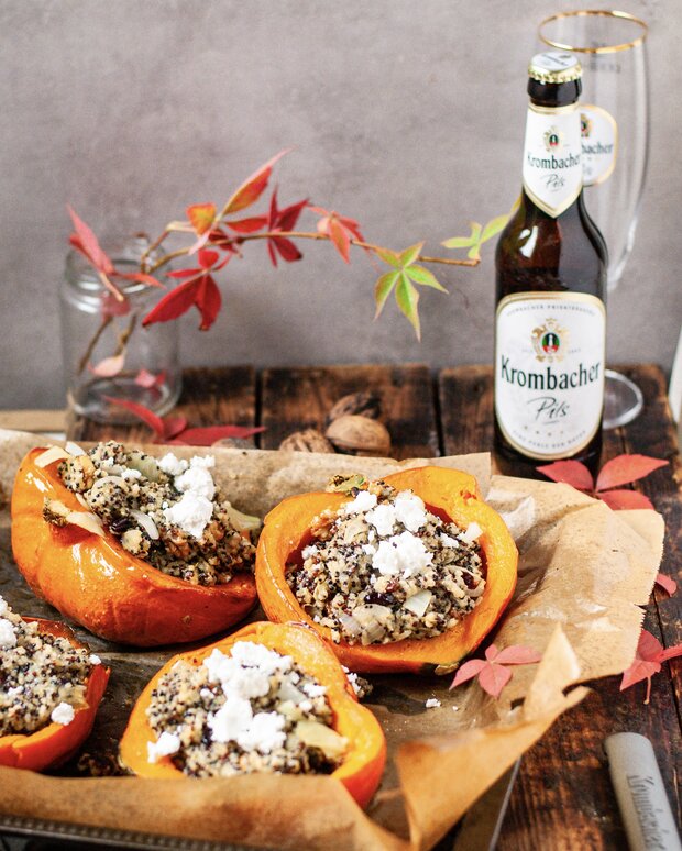 Ein gefüllter Kürbis auf einem Backpapier, umgeben von Walnüssen und herbstlichen Blättern.