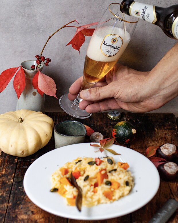 Über dem Teller Kürbisrisotto wird ein Glas Krombacher Pils eingeschenkt.
