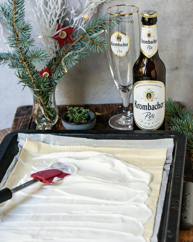 Ein Blech mit Blätterteig, auf dem eine weiße Creme verteilt wird. 