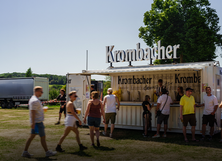 Mobiler Krombacher-Verkaufsstand mit mehreren Personen davor und im Freien bei sonnigem Wetter