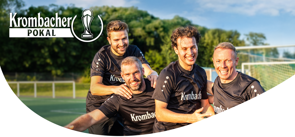 Vier Männer in schwarzen Krombacher-Trikots lachen und umarmen sich auf einem Fußballfeld im Freien.