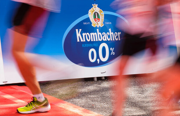 Werbung von Krombacher o,0% auf einer Bande, davor unscharfe Beine von zwei Läufern.