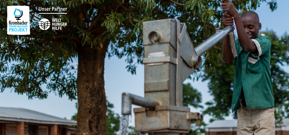 Ein junge in einem grünen Hemd pumpt Wasser aus einem Brunnen.
