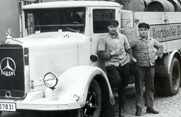 Historisches schwarz-weiß Foto von zwei Männern mit Mütze die vor einem Krombacher Lieferwagen stehen.
