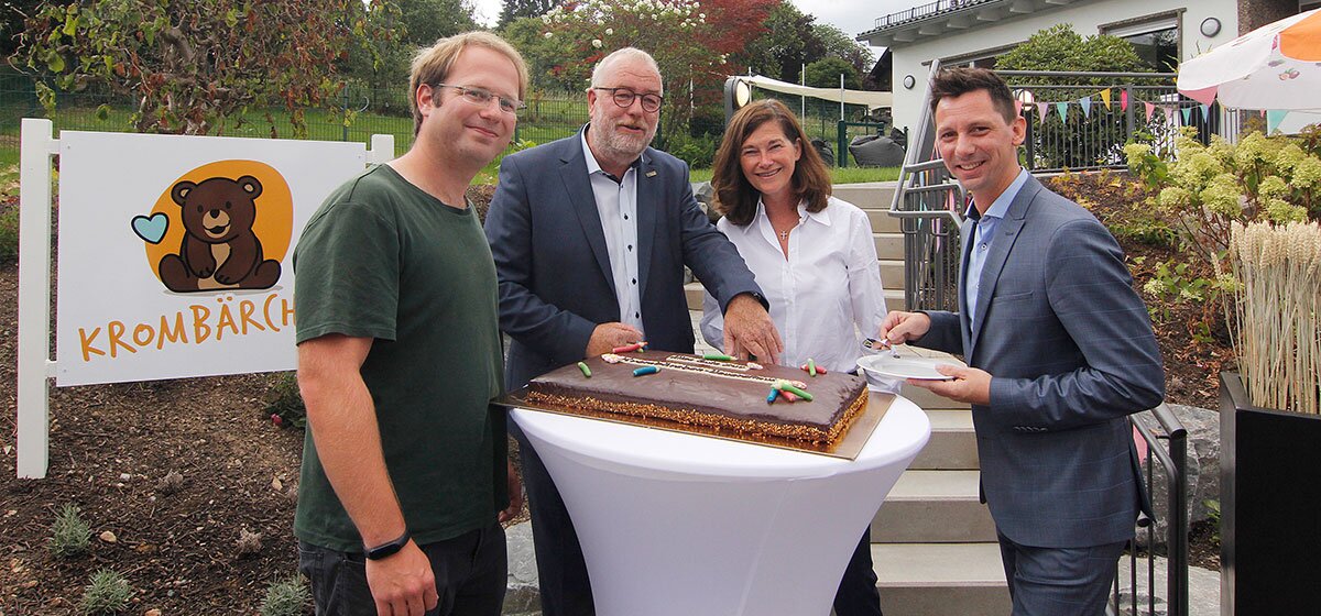 Vier Personen, darunter Frau Petra Schadeberg-Hermann (Geschäftsfühererin Krombacher Brauerei), stehen um einen Stehtisch mit einer großen rechteckigen Schokoladentorte, im Hintergrund ein Schild mit dem Krombärchen-Logo.