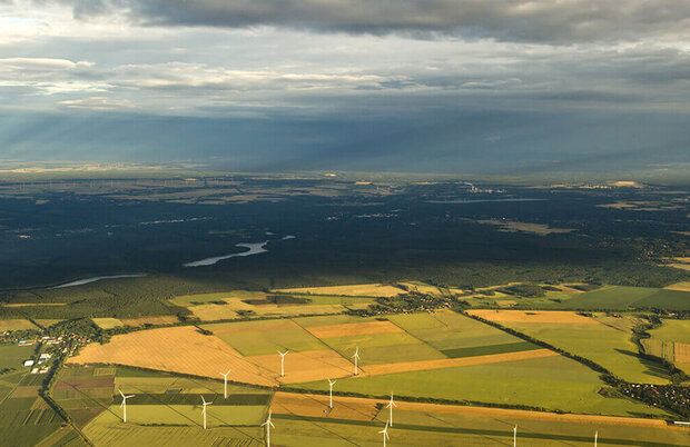 Luftaufnahme von Feldern mit mehreren Windrädern unter bewölktem Himmel.