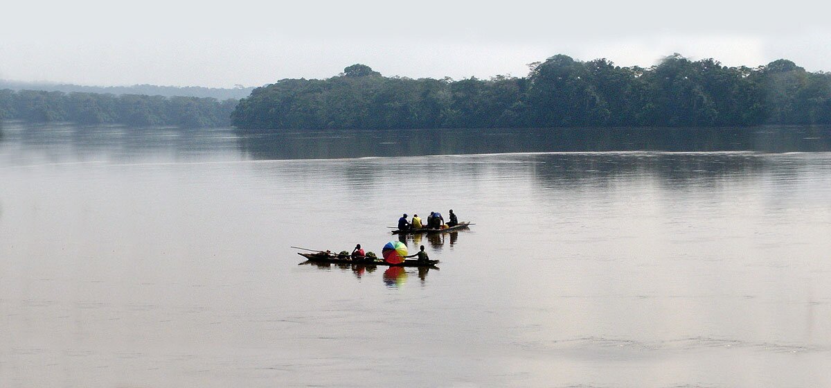 Fluss am Rande eines Regenwalds. Menschen fahren mit einem kleinen Booten auf dem Fluss.