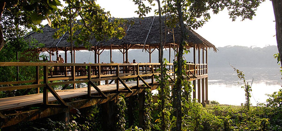 Abbildung der Shanga Lodge im Regenwald, direkt vor einem See.