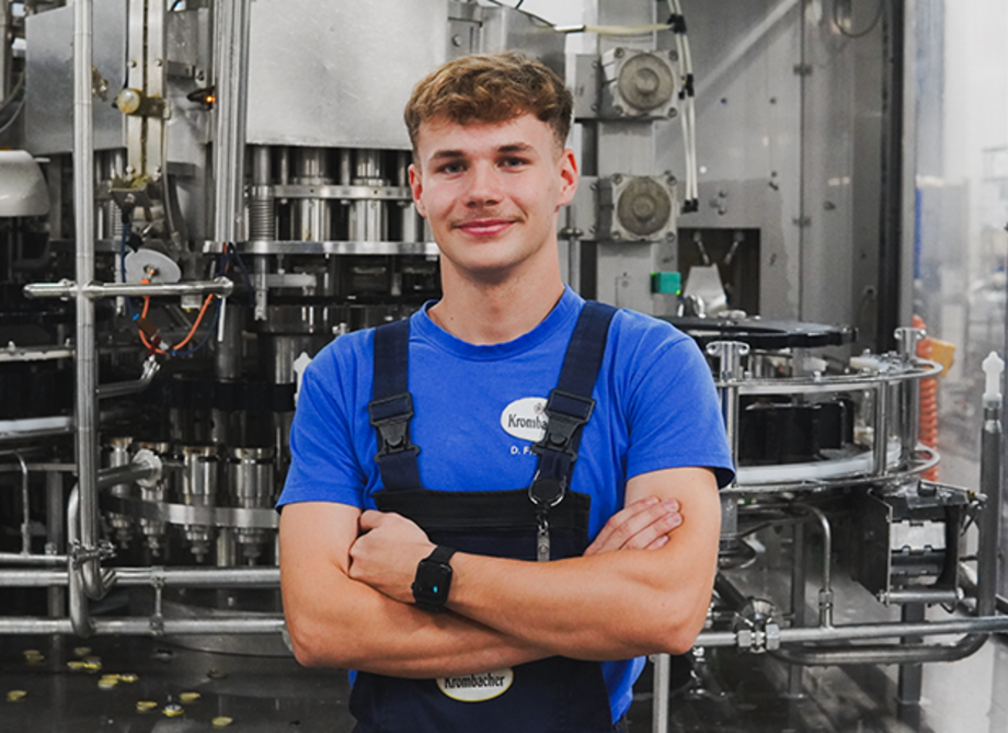 Mann mit dunkelblonden gelockten Haaren, trägt ein blaues T-Shirt und dunkelblaue Latzhose.