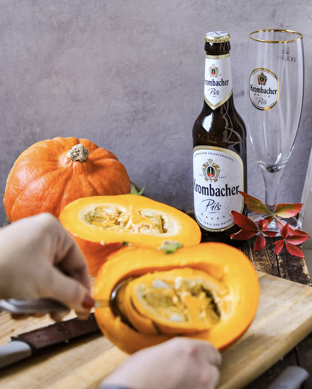 Ein Kürbis wird auf einem Holzbrett umgeben von Walnüssen und herbstlichen Blättern geschält.