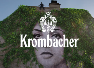 Ein Mann steht auf dem Dach eines Gebäudes, das mit grünen Pflanzen bewachsen ist. Im Vordergrund ist das Logo 'Krombacher' deutlich sichtbar.