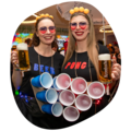 Zwei junge Frauen die Krombacher Bier in der Hand haben und als Beerpong-Tisch verkleidet sind.
