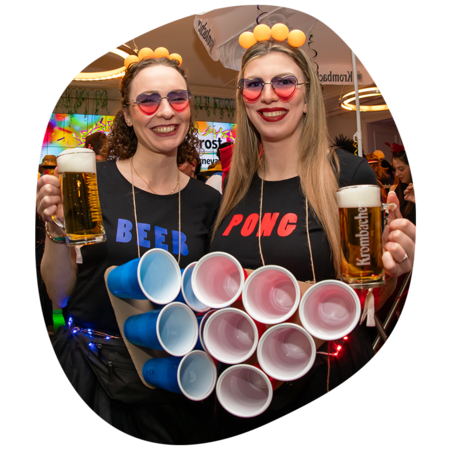 Zwei junge Frauen die Krombacher Bier in der Hand haben und als Beerpong-Tisch verkleidet sind.