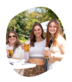 Drei junge Frauen stehen im Freien, halten Krombacher Seidel Biergläser und tragen ganz kleine Krombacher Schützenfest Hüte, eine trägt ein weißes Crop-Top und Leopardenmuster-Hose.