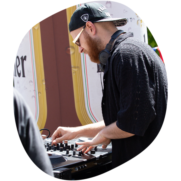 DJ mit schwarzer Kappe und Kopfhörern bedient Mischpult bei Sommerfest