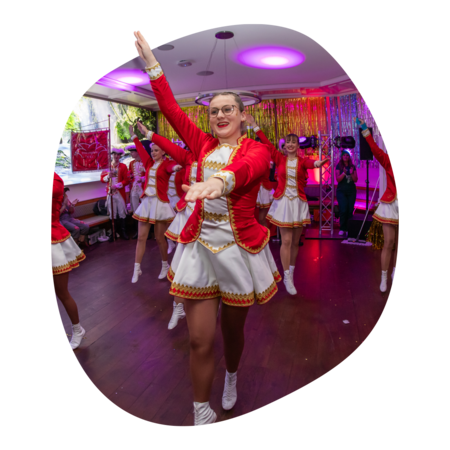 Tanzgruppe in roten und weißen Uniformen mit goldenen Verzierungen führt synchronen Tanz auf, Arme erhoben, in festlich dekoriertem Raum.