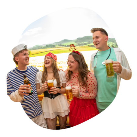 Vier Personen in Kostümen halten Biergläser, im Hintergrund Spannmotiv mit Feld mit Gerste.