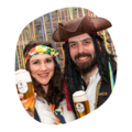Zwei Personen in bunter Kleidung, eine mit Piratenhut und Dreadlocks, halten Gläser mit Krombacher Pils im Glas vor buntem Hintergrund.