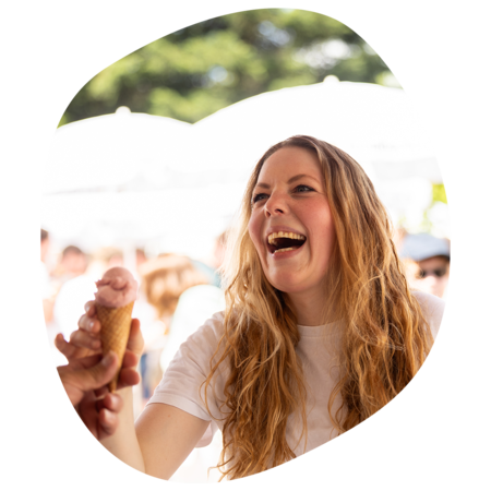 Junge Frau mit langen, gewellten Haaren reicht einem anderen ein Eis im Hörnchen bei sonnigem Sommerfest