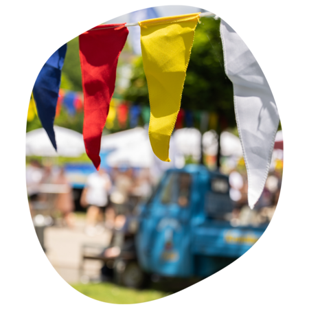 Bunte Wimpel in Rot, Gelb, Weiß und Blau beim Sommerfest mit unscharfem Hintergrund von Menschen und historischen Fahrzeugen