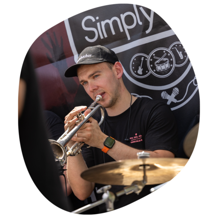 Mann mit schwarzer Kappe und T-Shirt spielt Trompete vor schwarzem Banner mit Logo von Simply Live